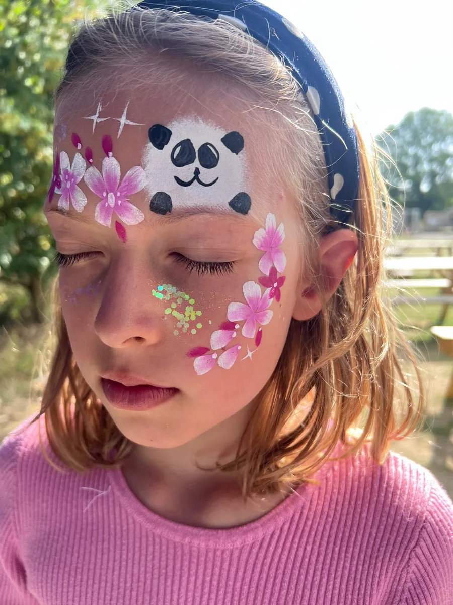 A panda painted on the forehead with pink and white blossom down the cheek and sparkling green glitter