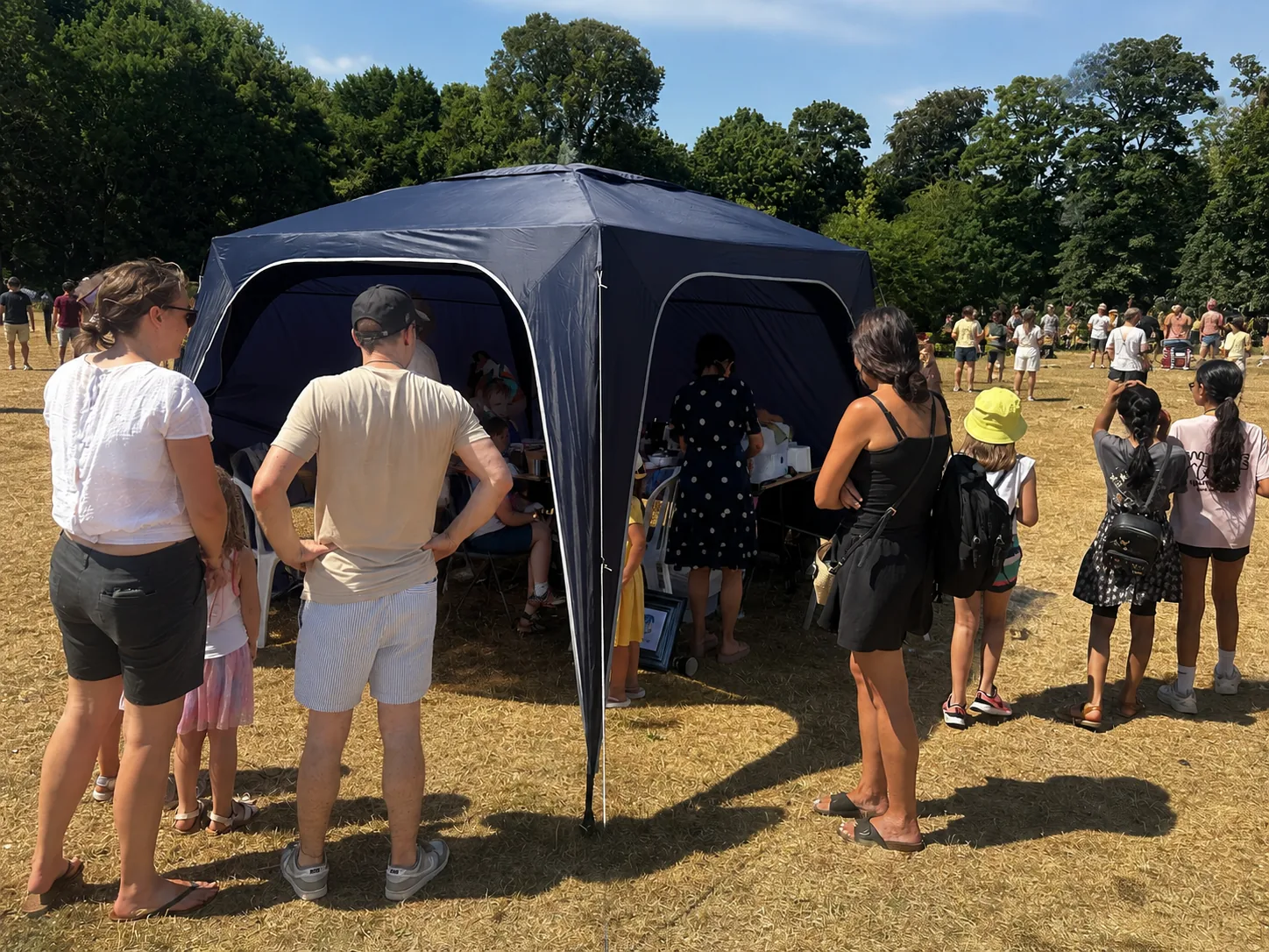 The Happy Harlequin's navy gazebo at a sunny local fete, with a small queue of visitors