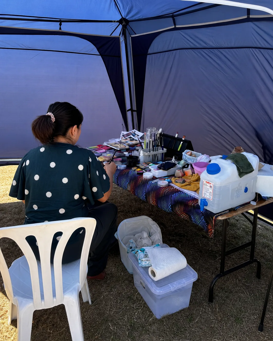 Face-painting brushes, paints and supplies arranged inside a navy gazebo